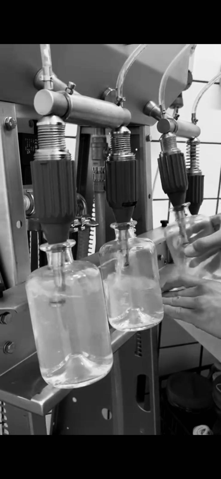 Macchina di riempimento che versa il distillato in bottiglie di vetro